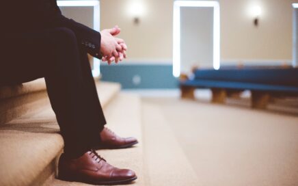 man in black pants and pair of brown leather lace-up shoes sitting on brown carpeted stairs inside room