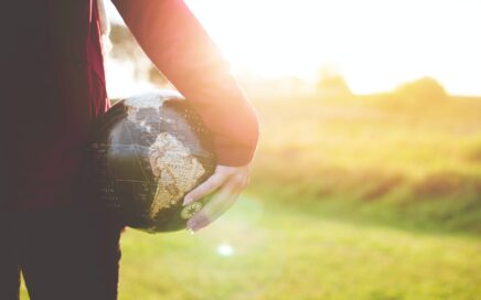 person holding black and brown globe ball while standing on grass land golden hour photography