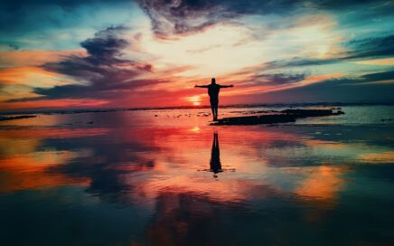 silhouette of person standing on rock surrounded by body of water