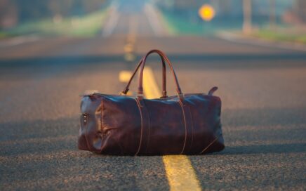 brown leather duffel bag in middle on gray asphalt road