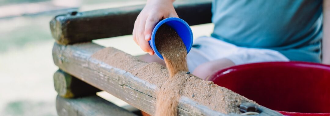 toddler pouring sand in brown wooden fence