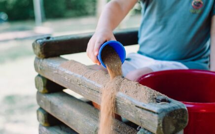 toddler pouring sand in brown wooden fence