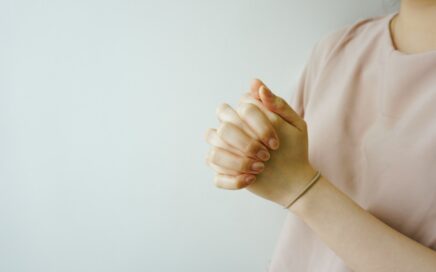 person wearing pink crew-neck shirt with hand clasped together