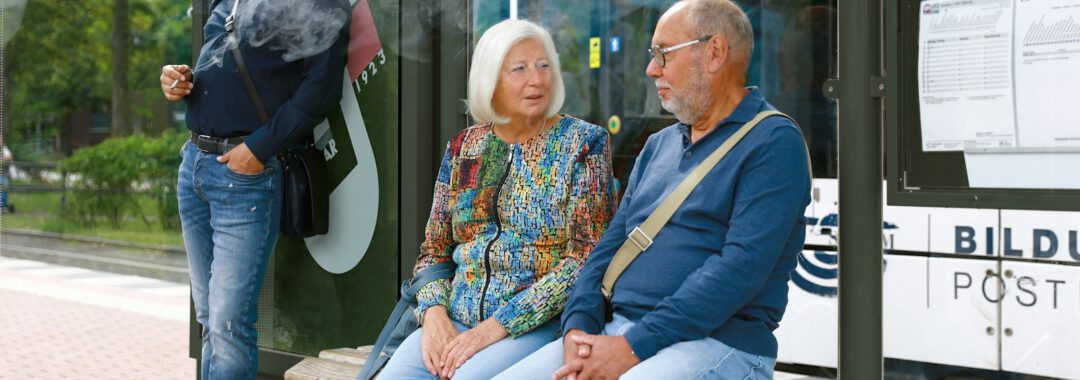 a man and woman sitting on a bench in front of a bus stop