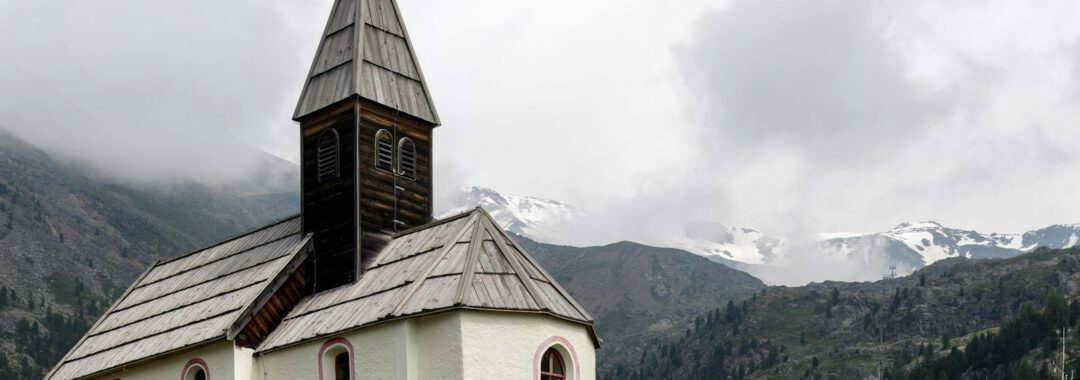 a small white church with a steeple on a grassy hill